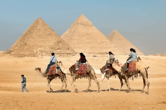 Tourist traveling on camel in Egypt with pyramid on the background